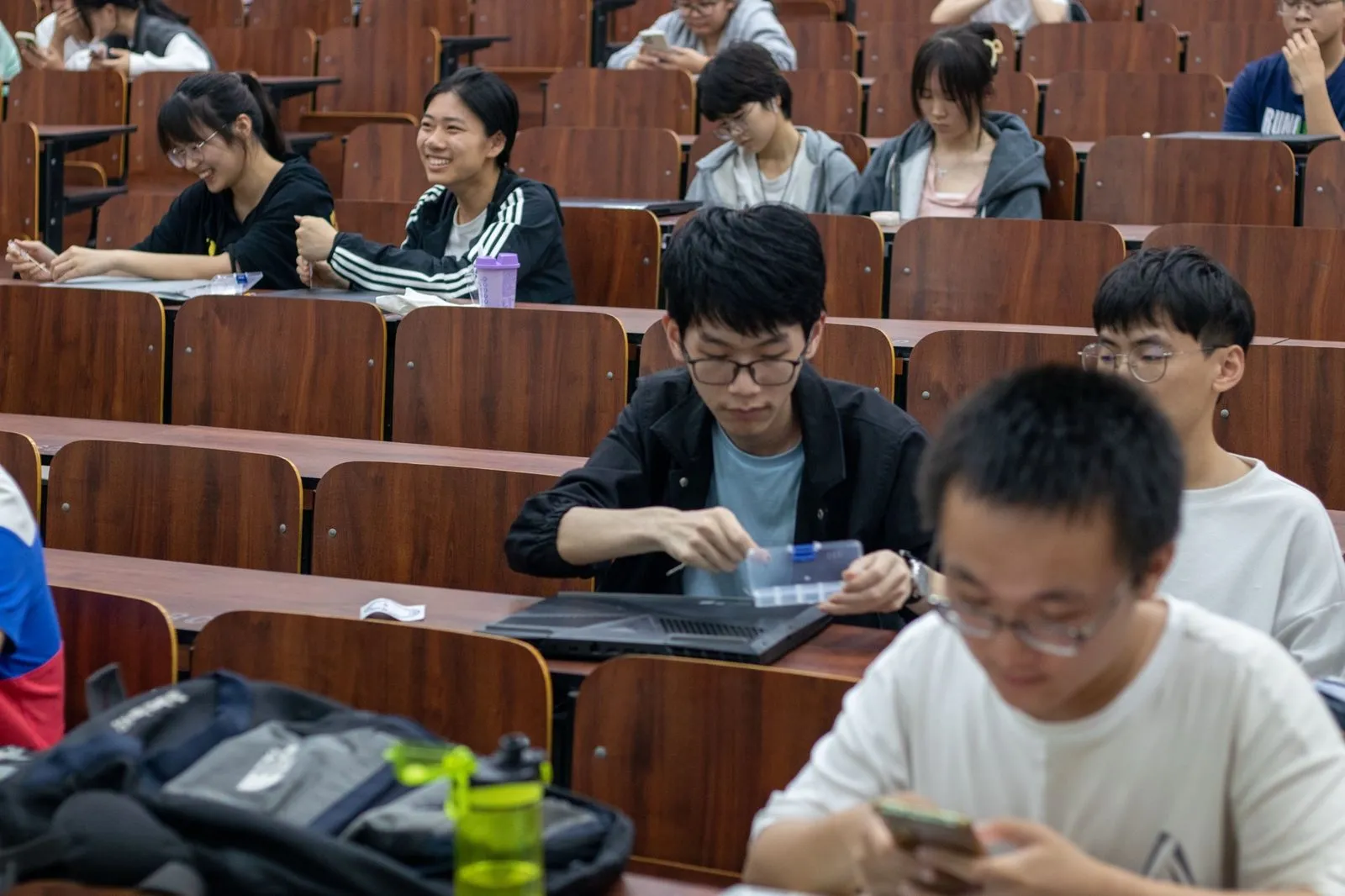 阶梯教室里的听众，一名同学正打开笔记本电脑、手里拿着零件收纳盒