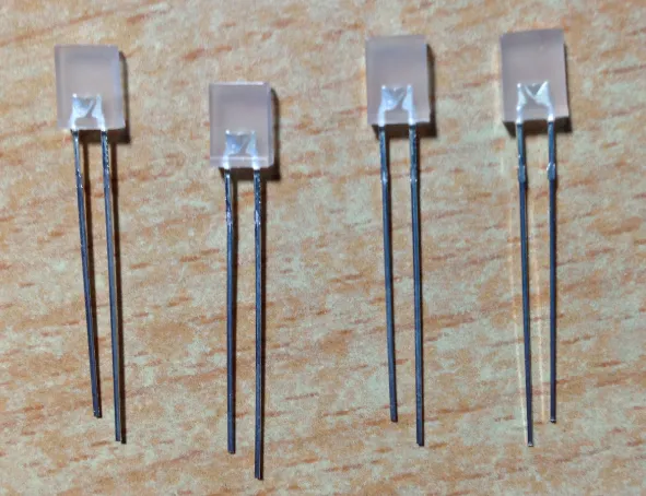 木纹桌面上并排四颗方形白色磨砂封装的 LED，引脚未剪，可见每颗都是一长一短两脚