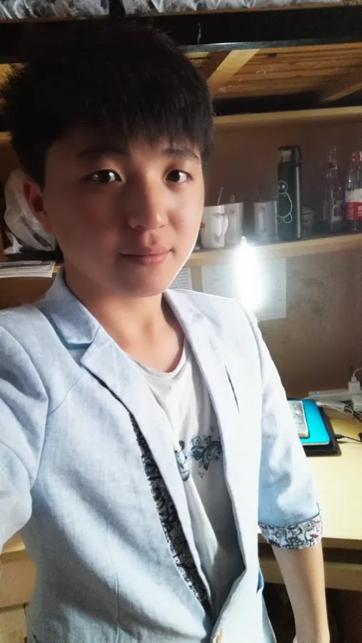 室内自拍：一名穿浅色外套的男生站在书桌前看向镜头