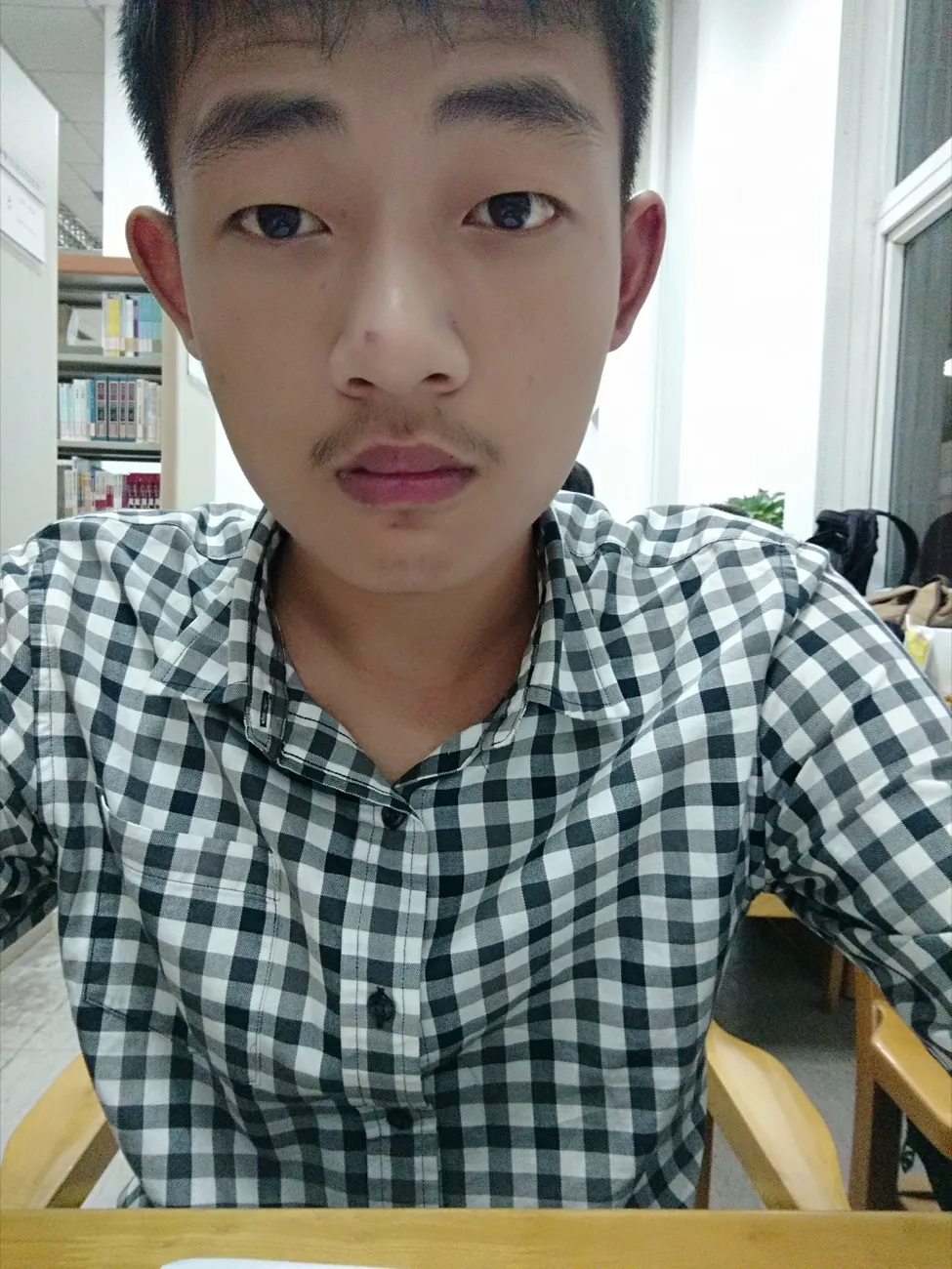 室内窗边的半身照，一名穿格子衬衫的男生正面对镜头